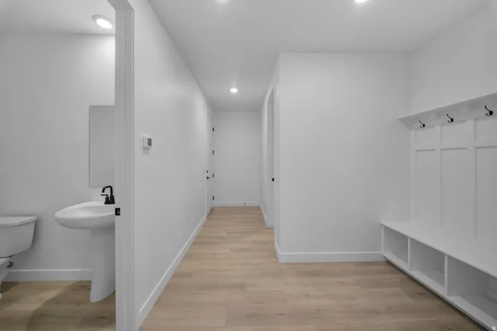 Recessed ceiling lighting, wood-finish flooring, built-in coat rack, built-in bench seating with storage, and a pedestal sink with a black matte faucet