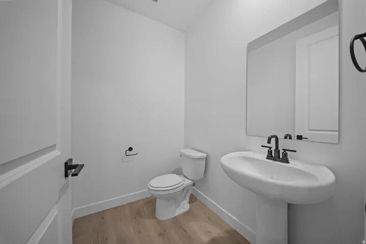 Pedestal sink with a matte black faucet, wall-mounted mirror, and wood-finish flooring