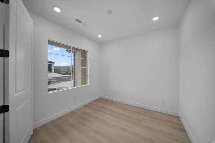 Bright room featuring a large window with grid panes, recessed ceiling lighting, a solid panel door with dark hardware, and wood-finish flooring