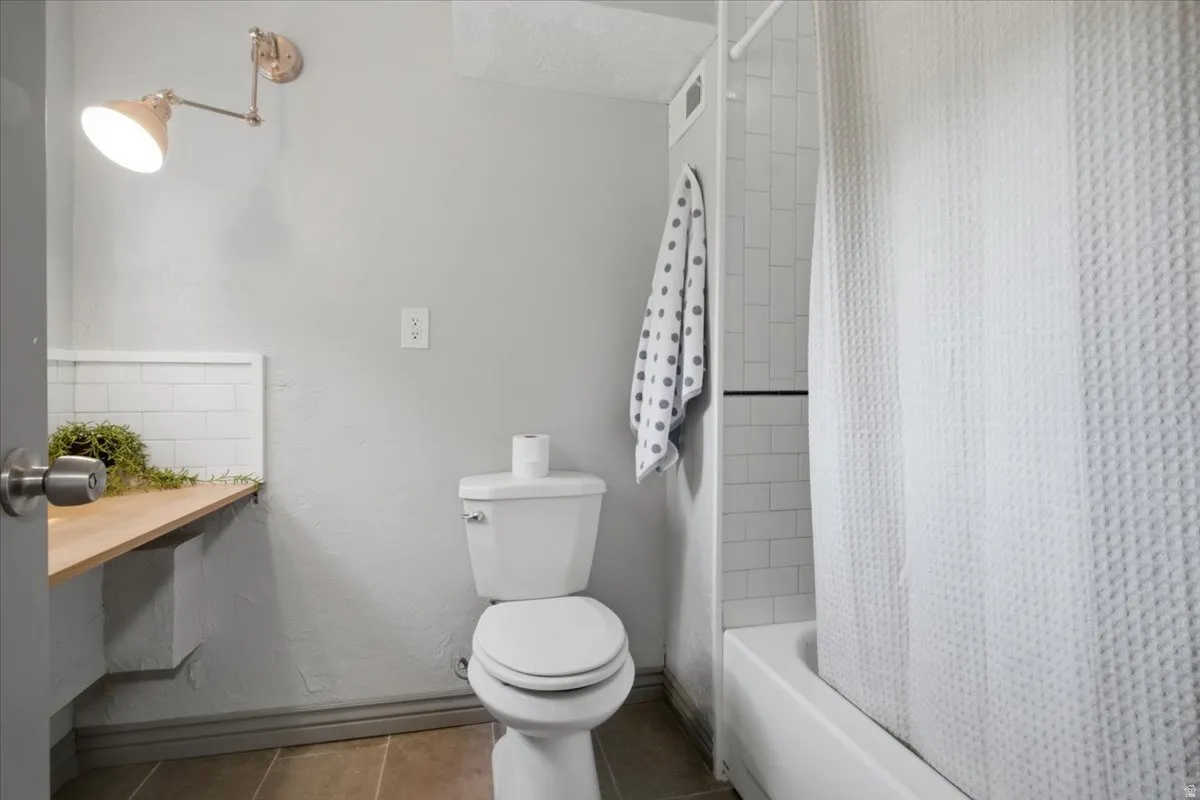 Built-in wood-finish shelving with subway tile backsplash, wall-mounted adjustable sconce, and a tub and shower combination with subway tile surround