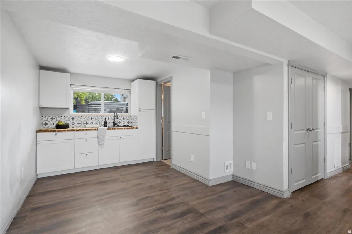 Kitchenette featuring white cabinetry, a farmhouse-style sink with a matte black faucet, patterned tile backsplash, and wood-finish flooring