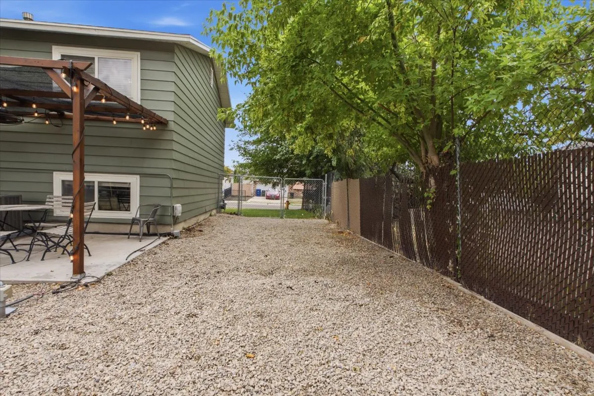Spacious gravel yard with perimeter fencing, a concrete patio, and a wood pergola structure
