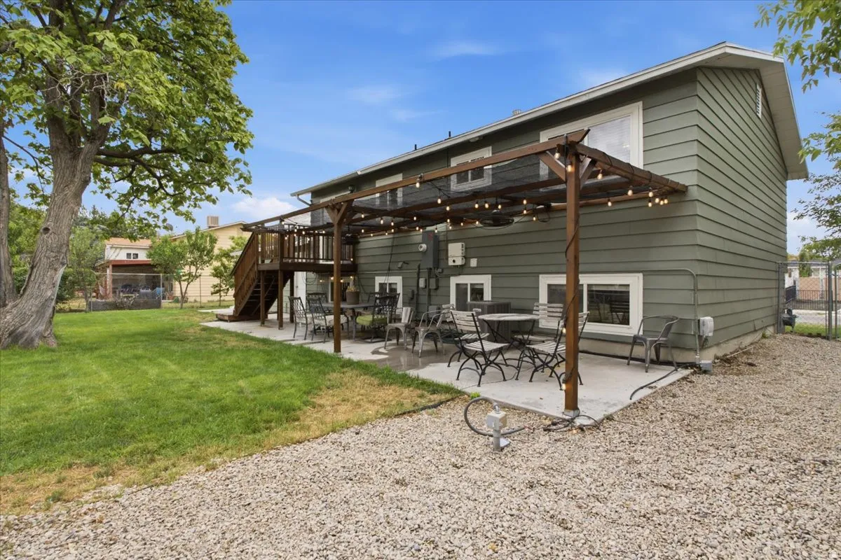 Expansive concrete patio with a wooden pergola structure, a gravel-covered area, and a large grassy yard