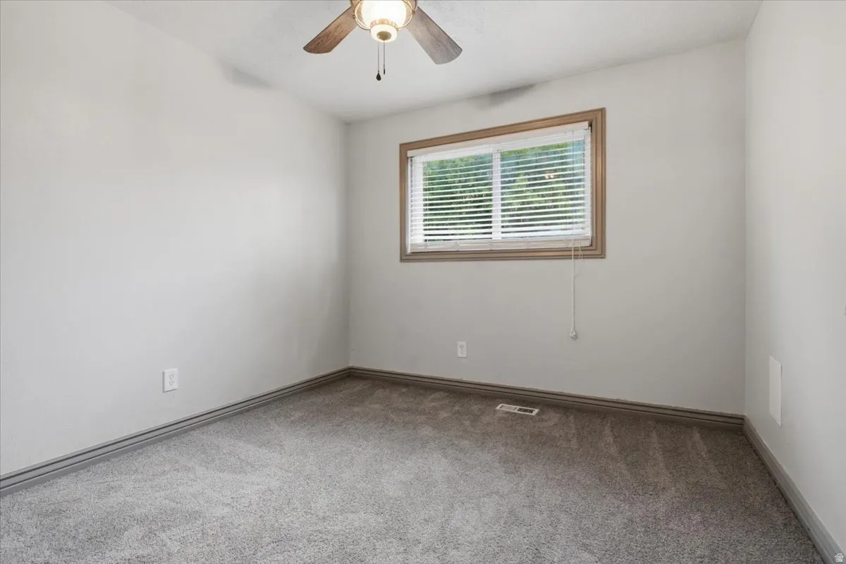 Plush carpet flooring, wood-framed window with blinds, ceiling fan, and neutral wall tones