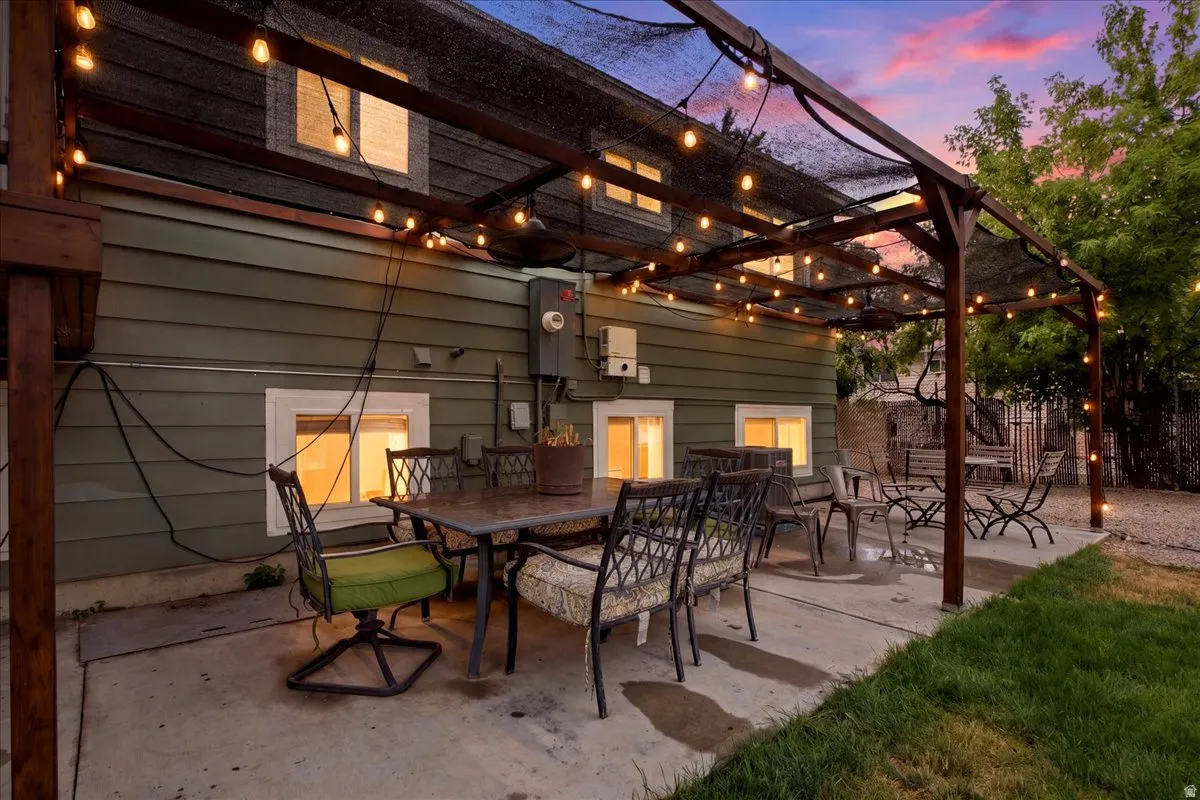 Concrete patio with a wood pergola, string lighting, and a mesh shade cover