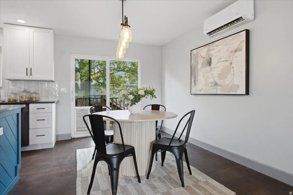 White cabinetry with dark hardware, dark countertops, wood-finish flooring, sliding glass door, and wall-mounted climate control unit