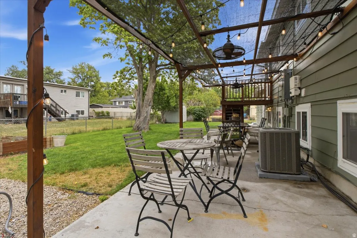 Covered patio with string lighting and ceiling fan, featuring a concrete surface and a partial privacy screen