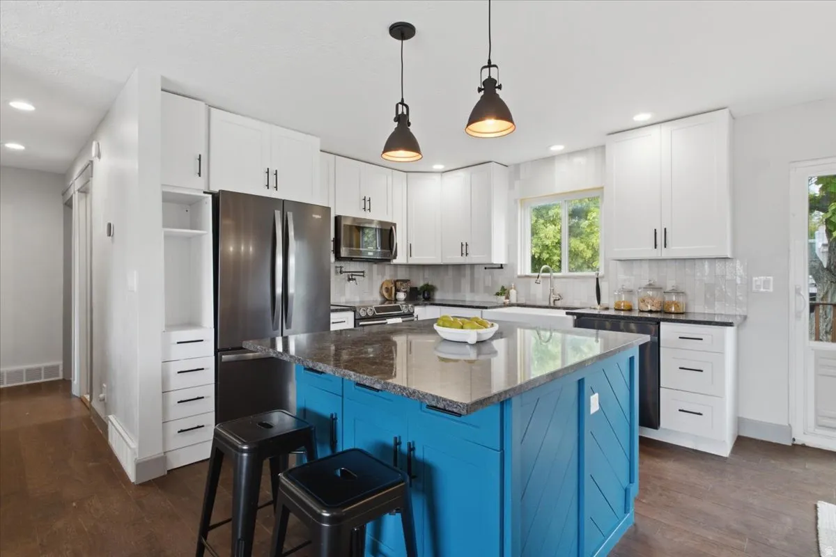 Kitchen featuring a central island with a stone countertop, white shaker-style cabinetry, and stainless steel appliances