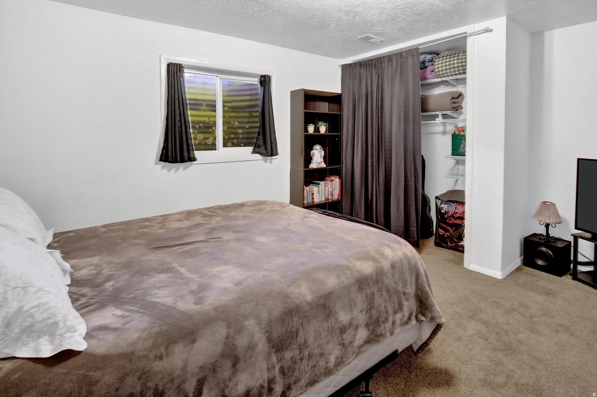Carpeted bedroom featuring a built-in closet with shelving, a window, and a built-in shelving unit