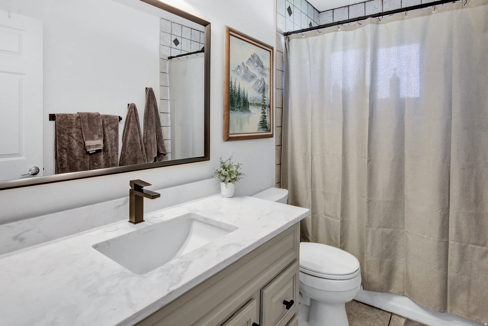 Vanity with integrated sink and stone-finish countertop, bronze-finish faucet, and coordinating framed mirror