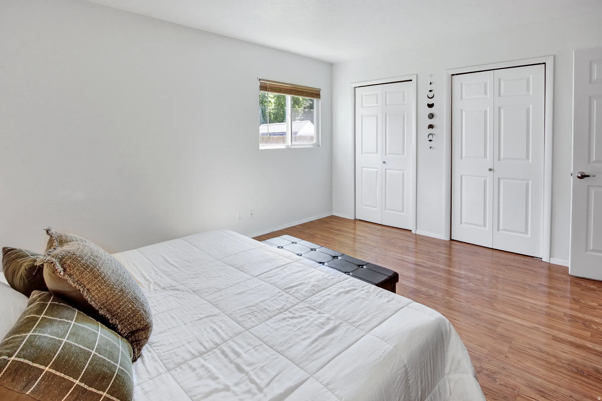 Light-filled room featuring wood-finish flooring, a window with blinds, and two sets of bi-fold closet doors