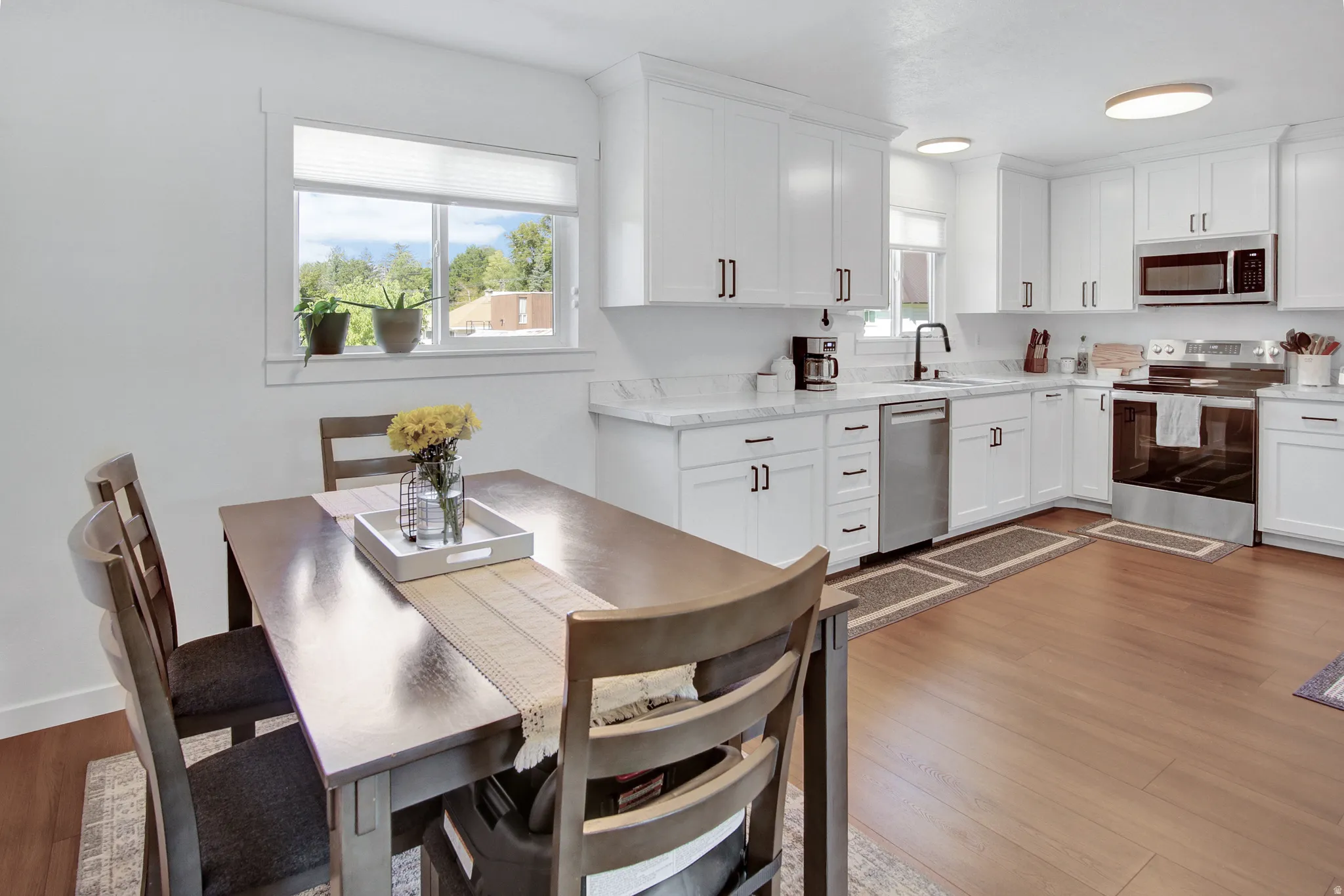 Kitchen featuring white cabinetry, stainless steel appliances, light-toned countertops, wood-finish flooring, and a dining area