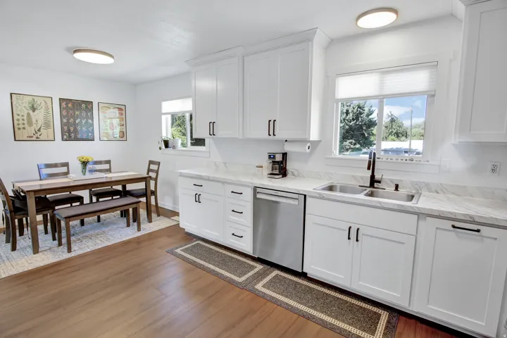 Kitchen featuring white shaker cabinetry, stainless steel appliances, stone-finish countertops, wood-finish flooring, and a dining area