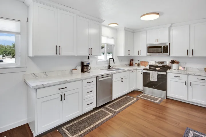 White shaker-style cabinetry with black hardware, wood-finish flooring, stainless steel appliances, and light-toned countertops