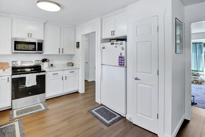Kitchen featuring white shaker cabinetry, stainless steel microwave, stainless steel range, light-toned countertops, and wood-finish flooring