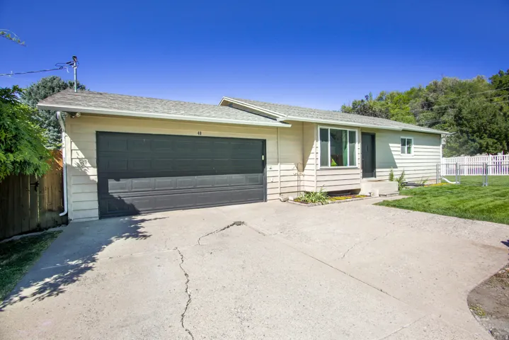 Single-story residence featuring siding exterior, an attached garage, a concrete driveway, and a white picket fence enclosing a portion of the yard