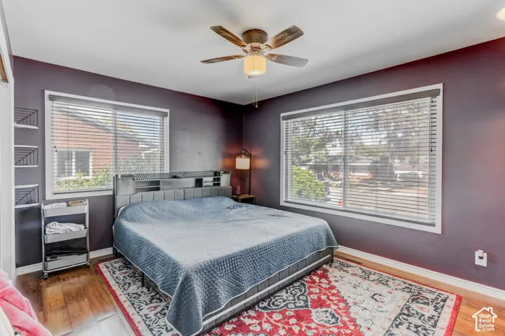 Wood-finish flooring, dual windows with blinds, ceiling fan, and built-in shelving