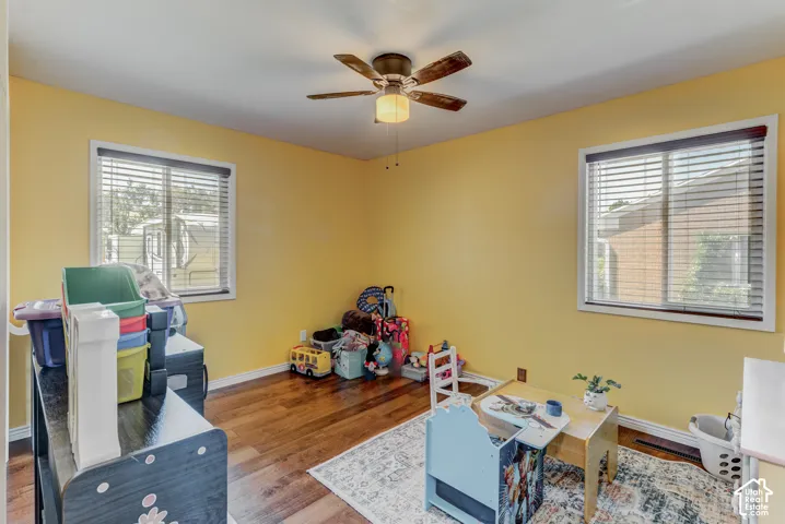 Room featuring wood-finish flooring, two windows with blinds, and a ceiling fan with integrated lighting