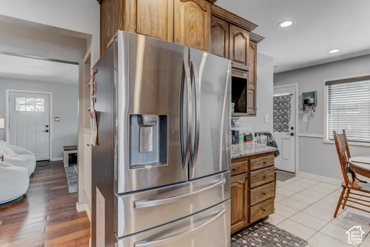 Stainless steel French door refrigerator, wood-finish cabinetry, granite-style countertops, tile flooring, recessed lighting