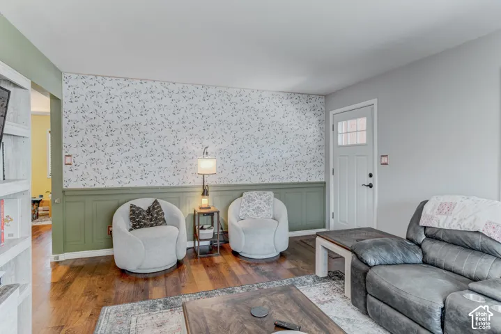 Hardwood-finish flooring, half-wall paneling, patterned wall covering, and a white entrance door with divided lites