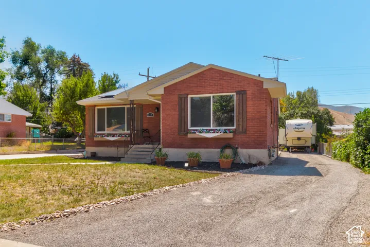 Brick-clad exterior with a covered entry, front porch with railings, and a gravel driveway