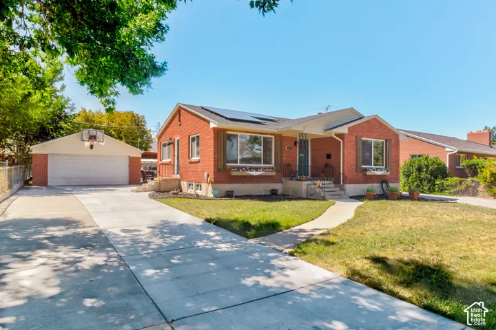 Red brick exterior with white trim, a covered porch, an attached garage, a detached garage, and solar panels