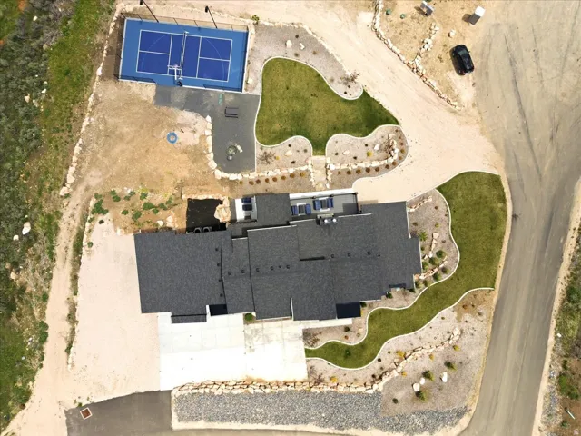 Expansive paved driveway, attached sport court, landscaped grounds with green lawn, and solar panels