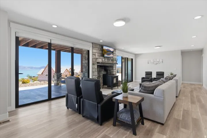 Expansive sliding glass doors, stone fireplace with a wood-burning stove, light wood-finish flooring, recessed lighting, and a modern ceiling fixture