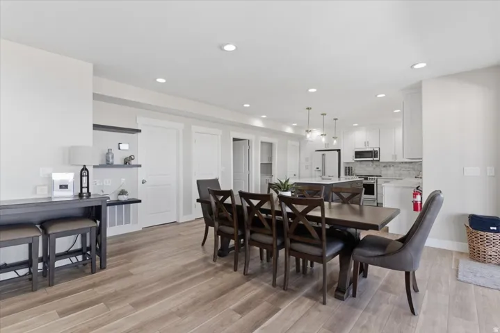 Wood-finish flooring throughout, recessed lighting, white shaker cabinetry, stainless steel appliances, and a kitchen island with seating