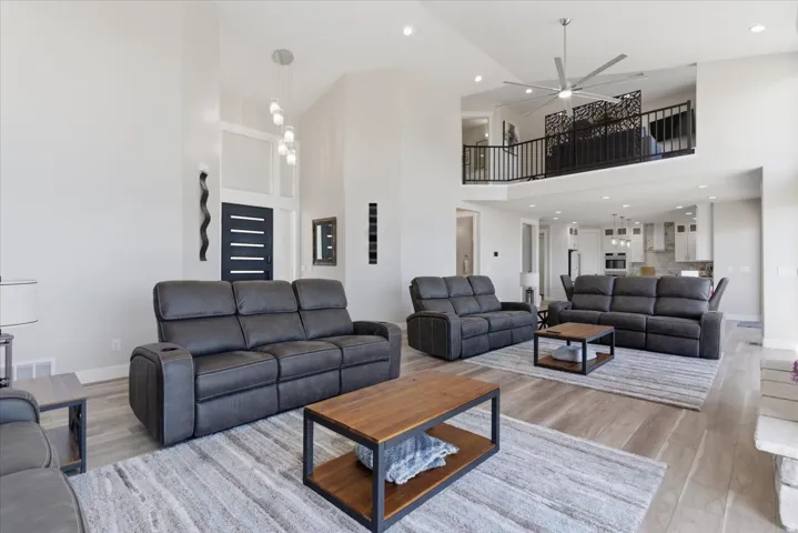 Spacious living area featuring vaulted ceilings, wood-finish flooring, an open-concept layout, a balcony with decorative railing, and recessed lighting