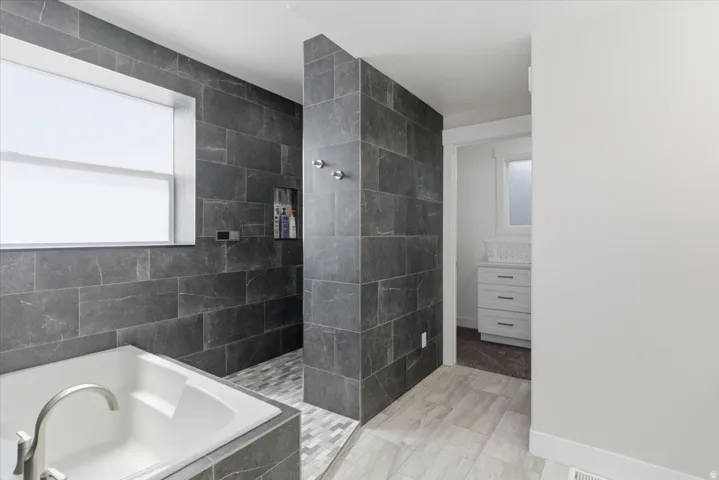 Soaking tub with brushed nickel fixtures, dark tile surround, and a window