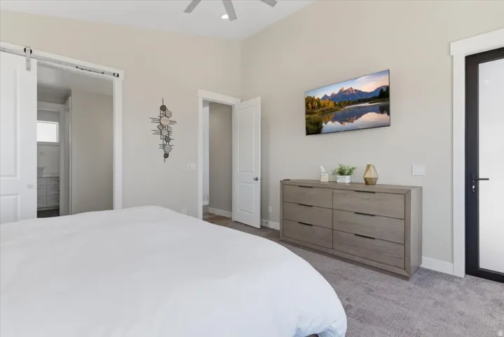Vaulted ceiling with a ceiling fan, carpeted flooring, and a sliding barn door