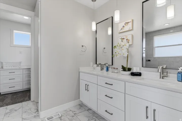 Dual vanity with white cabinetry and countertops, framed mirrors, and pendant lighting