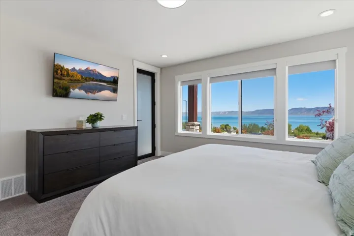 Three large windows with roller shades, a ceiling-mounted light fixture, recessed lighting, and a dark wood-finish dresser with six drawers