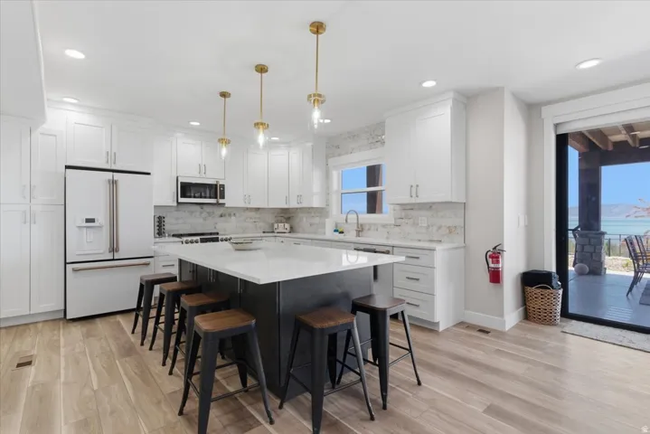 White cabinetry with brushed nickel hardware, expansive center island with seating, wood-finish flooring, recessed lighting, and sliding glass door with outdoor patio access
