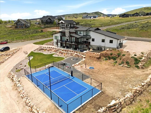 Multi-level residence featuring extensive outdoor living space, a full-size sports court, terraced landscaping, and a substantial stone chimney