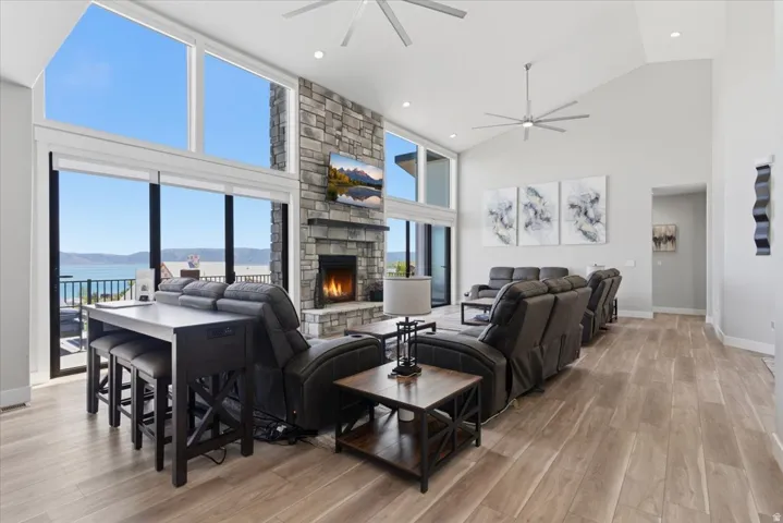Vaulted ceilings with recessed lighting, floor-to-ceiling windows, stone fireplace with a built-in mantel, and wood-finish flooring