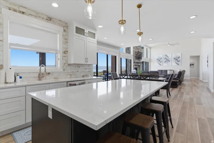 Open-concept living space with a large kitchen island, recessed lighting, wood-finish flooring, white cabinetry, and abundant natural light