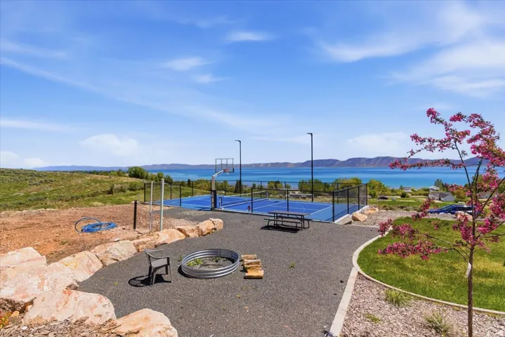 Sport court with perimeter fencing, fire pit area, natural rock landscaping, and water backdrop