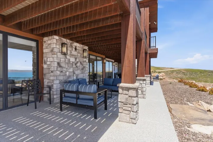 Ground-level patio with stone veneer wall, expansive sliding glass doors, exposed wood beams, and a concrete surface