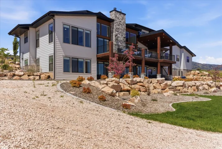 Contemporary exterior with multi-level decks, a stone chimney, extensive rock retaining walls, and a sloped gravel and grass landscape