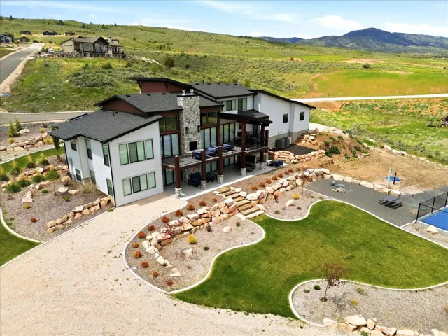 Contemporary exterior with stone accents, extensive multi-level decking, a lower-level patio, a gravel driveway, and landscaped grounds