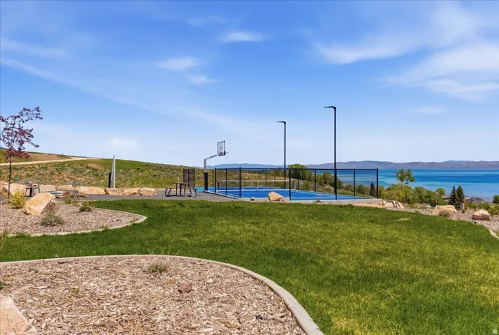 Manicured lawn with landscaped beds, sports court with basketball hoop, integrated lighting fixtures, and distant body of water