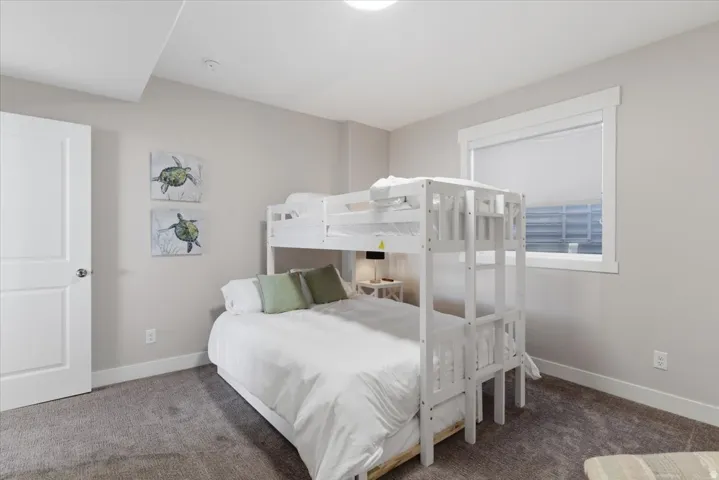 Neutral tone walls, white trim, window with roller shade, bunk bed, and carpeted flooring