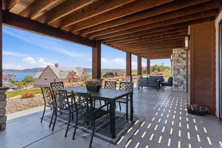 Expansive covered patio featuring an exposed wood beam ceiling, stone-clad columns, and a concrete patio surface