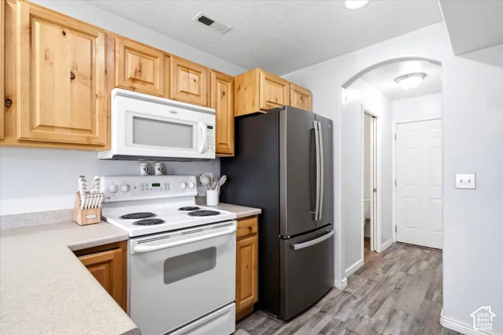 Kitchen featuring wood cabinetry, light-toned countertops, a white electric range, and a stainless steel refrigerator
