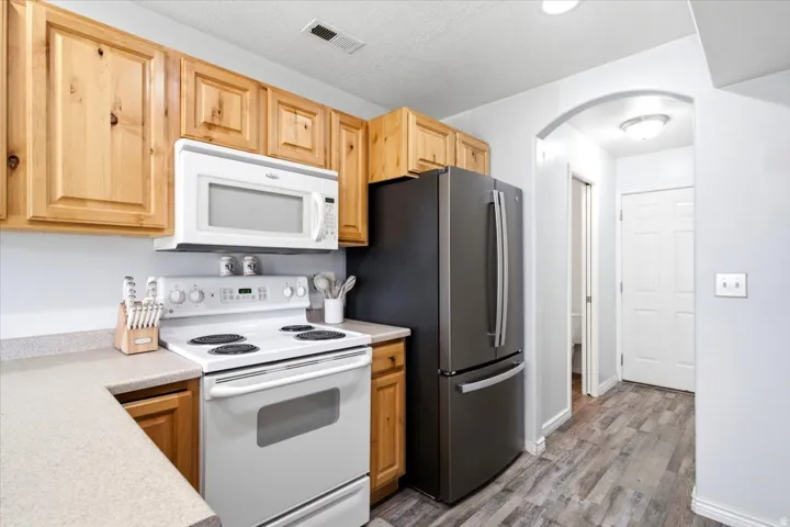 Kitchen featuring wood cabinetry, light-toned countertops, a white electric range, and a stainless steel refrigerator
