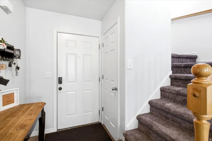 Panel-style entry door, wood-finish flooring, paneled interior door, carpeted staircase, and wood newel post