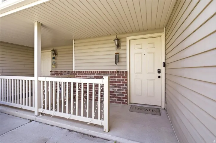 Covered porch with wood-finish railing, brick accent wall, and exterior lighting fixture