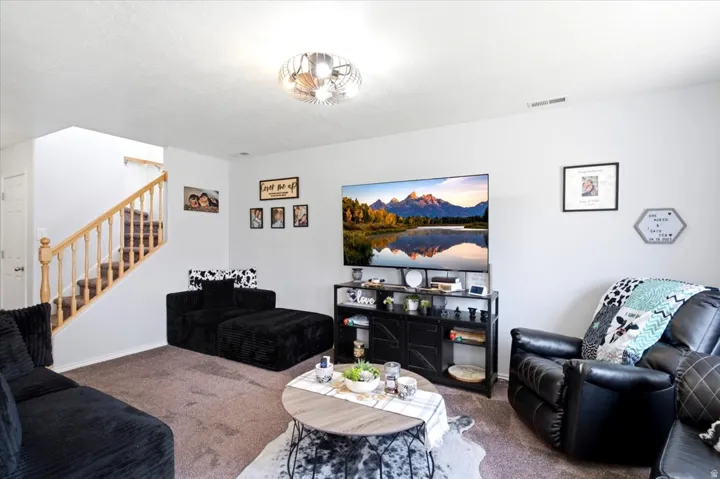 Carpeted living area with light-toned walls, a built-in stairwell with wood railings, and an overhead flush-mount light fixture